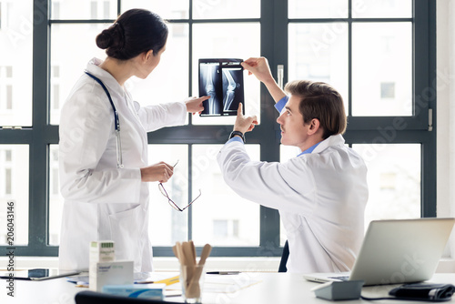 Experienced male orthopedist helping his female colleague with the interpretation of an X-ray of the knee of a patient in the office