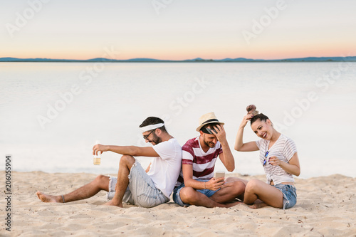 Group of happy young people sitting together at the beach and taking selfie