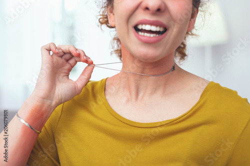 Low-quality metal. Young lady looking sore and unwell while holding on to her low-quality necklace causing her skin have allergic response