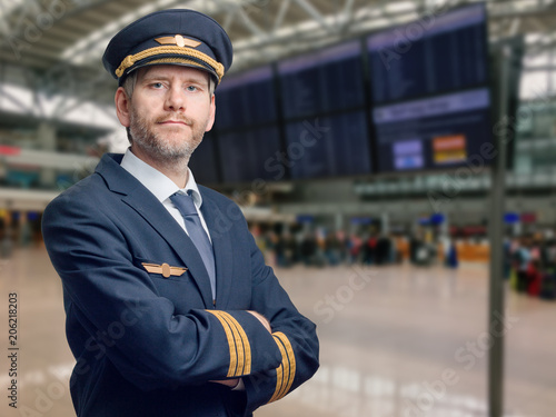 Pilot in der Uniform mit goldenen Streifen und Kappe kreuzte seine Arme beim Stehen im Flughafen