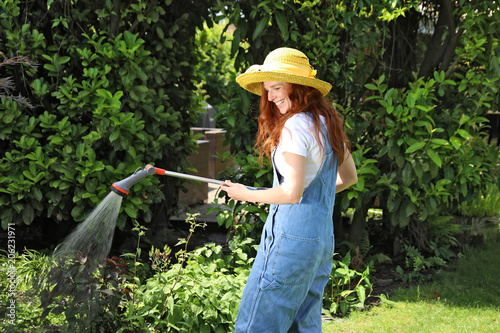 Hübsche rothaarige Frau bei der Gartenarbeit wässert mit einer Brause ein Beet