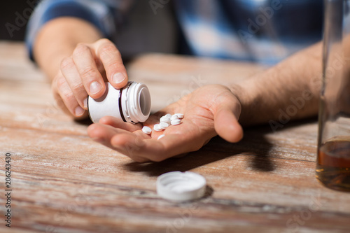 depression, drug abuse and addiction people concept - unhappy drunk man with bottle of alcohol and pills committing suicide by overdosing on medication at night