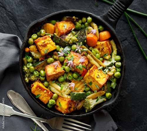 Tofu with vegetables sprinkled with herbs and edible flowers, top view. Vegan dish delicious and nutritious. Healthy eating concept