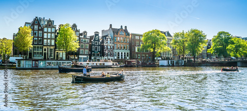 Amsterdam, May 7 2018 - view on the river Amstel filled with small boats and traditional houses in the background on a summer day