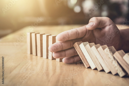 Strategy and successful intervention concept for business, businessman hand Stopping Falling wooden Dominoes effect from continuous toppled or risk