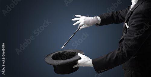 Illusionist white hand wants to conjure with magic wand from a black cylinder something