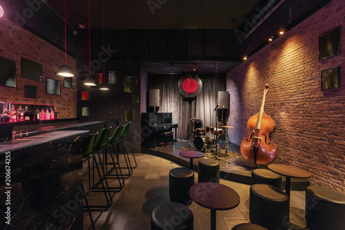 Modern jazz bar interior design, stage with black piano and cello, lamps above bar counter