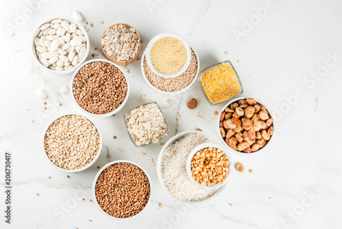 Selection various types cereal grains groats in different bowl on white marble background, copy space top view