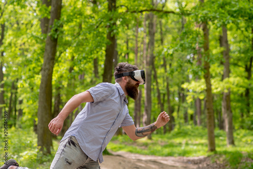 Bearded man having 3D experience wearing VR headset. Side view hipster in forest. Man running in virtual reality, modern gadgets, digital world concept