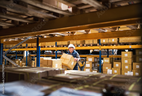 Senior male warehouse worker or a supervisor unloading a pallet truck with boxes.