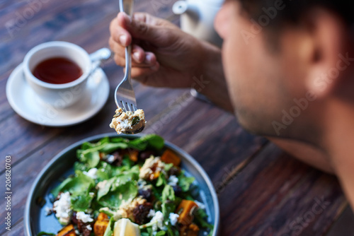 Man eating delicious salad while sitting at a bistro table