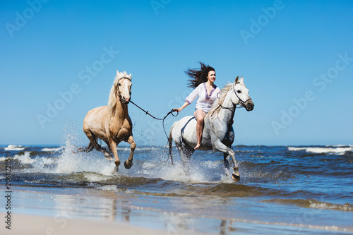 Girl galopading through the sea with two horses.