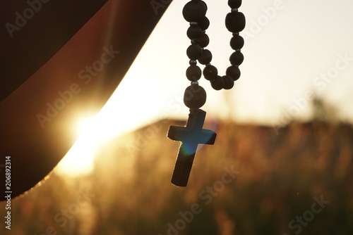 Silhouette of girl hands praying with rosary at sunset