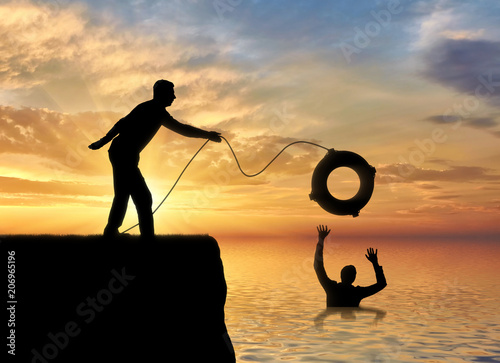 A silhouette of a man throws a lifeline to another man who is drowning in the water