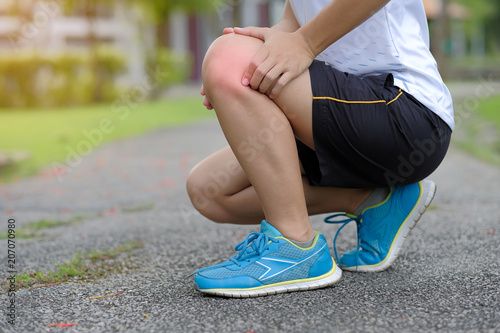 Young fitness woman holding her sports leg injury, muscle painful during training. Asian runner having knee ache and problem after running and exercise outside in summer