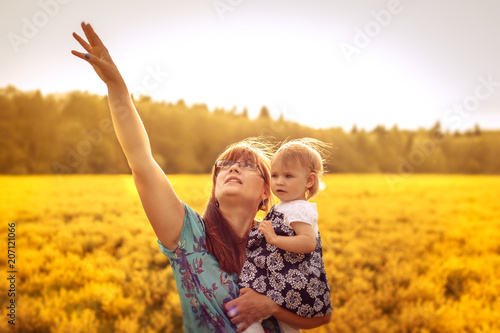 Happy mother with baby in a yellow field at sunset.