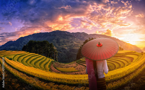 Woman holding traditional red umbrella on Rice fields terraced with pine tree at sunset in Mu Cang Chai, YenBai, Vietnam.