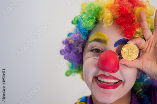 Smiling clown holding a Bitcoin coin in the direction of his eyes