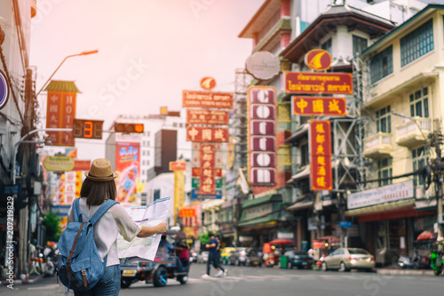 Young asian woman traveler with blue backpack and hipster hat looking map on road with tuk tuk Thailand background at China Town Bangkok. Traveling in Bangkok Thailand