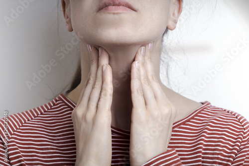 A woman is holding her hands on a sore throat.