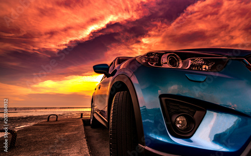 Blue compact SUV car with sport, modern, and luxury design parked on concrete road by the sea at sunset. Front view of beautiful hybrid car. Driving with confidence. Travel on vacation at the beach.