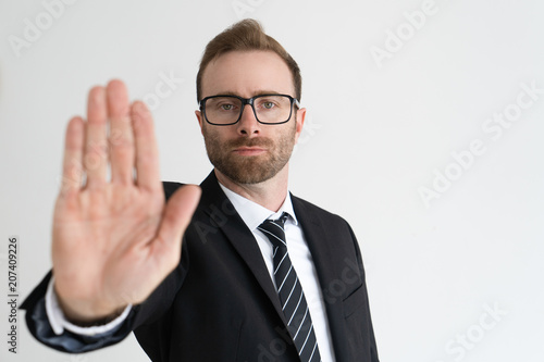 Serious business man showing open palm or stop gesture and looking at camera. Restriction concept. Isolated front view on white background.