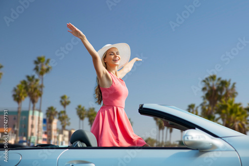 travel, summer holidays, road trip and people concept - happy young woman wearing hat in convertible car enjoying sun over venice beach background in california