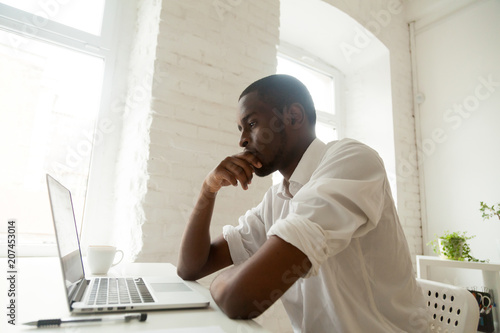 Focused thoughtful African American worker looking at laptop screen, heavily thinking about problem solution, analyzing possible variants, calculating risks, striving for business success motivation