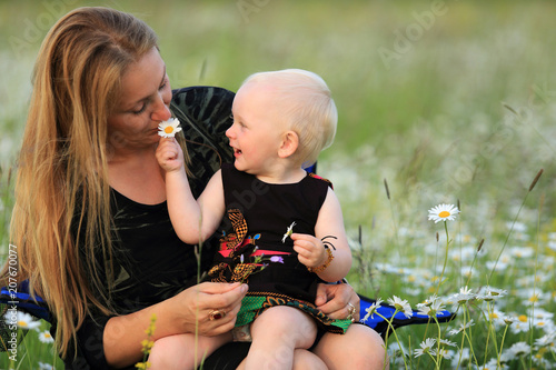 Mała dziewczynka bawi się z matką kwiatkami na łące.
