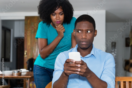 Jealousy african american woman checking chat on cellphone of boyfriend