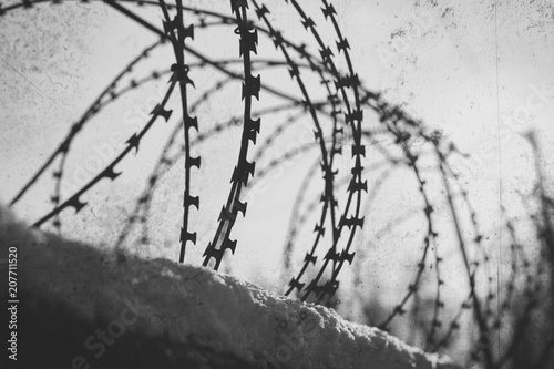 Barbed wire stretches along the concrete wall. Black and white photo