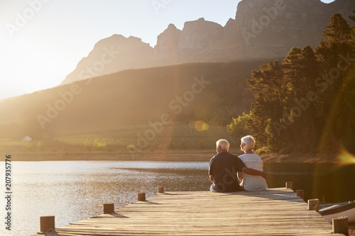 Romantic Senior Couple Sitting On Wooden Jetty By Lake