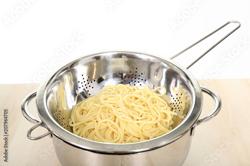 Ugotowany makaron spagetti odcedzony na metalowym durszlaku, sitku.