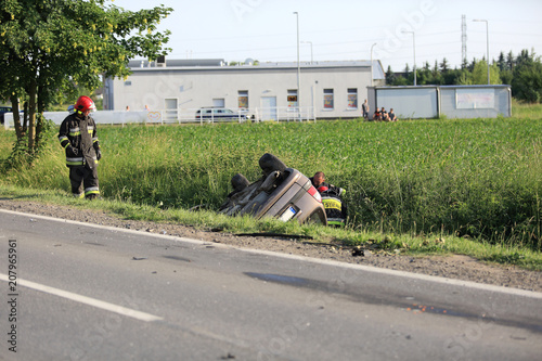 Wypadek samochodowy, strażacy przy aucie leżącym w rowie kołami do góry.