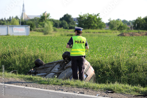 Policjantka wykonuje czynności przy aucie leżącym w rowie kołami do góry.