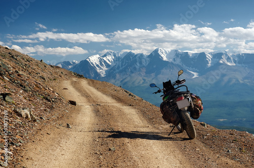 Motorcycle enduro traveler with suitcases standing alone on yellow stone extreme road path on the background of high snow glacier ranges Altai mountains Siberia Russia