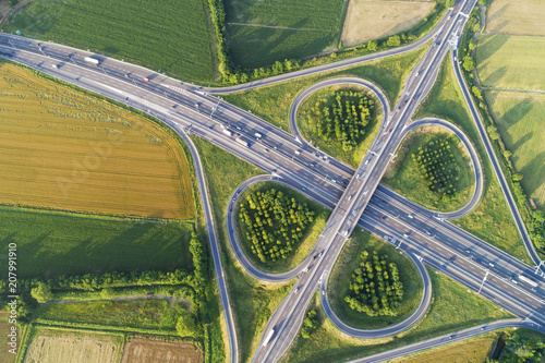 Cloverleaf interchange seen from above. Aerial view of highway road junction in the countryside with trees and cultivated fields. Bird's eye view.