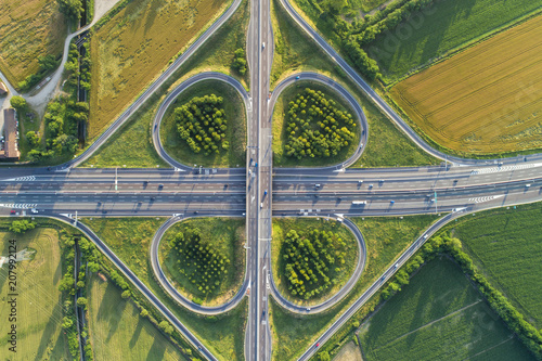 Cloverleaf interchange seen from above. Aerial view of highway road junction in the countryside with trees and cultivated fields. Bird's eye view.