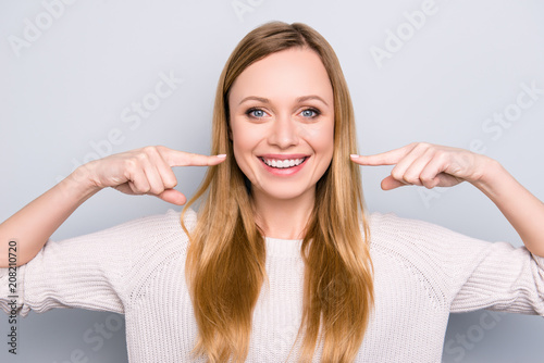 Portret radosna zadowolona dziewczyna gestykuluje jej promieniejących białych zdrowych zęby z dwa palcami wskazującymi patrzeje kamerę odizolowywającą na szarym tle. Koncepcja ortodontyczna