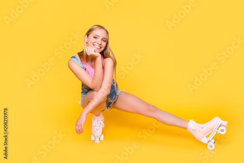 Portrait of cheerful charming girl sitting on roller skates making break time out pause looking at camera isolated on yellow background