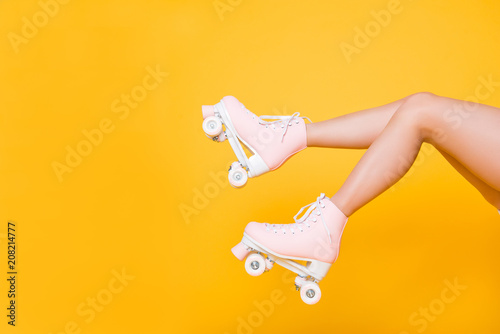 Cropped portrait of legs in pink vintage quad roller skates shoes isolated on yellow background, extreme balance concept, street outside urban lifestyle style, laser hair removal perfect skin