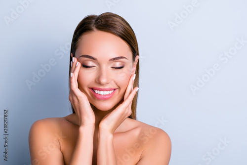 Portrait of pleased satisfied girl touching face enjoying ideal perfect skin after procedure mask keeping eyes closed isolated on grey background