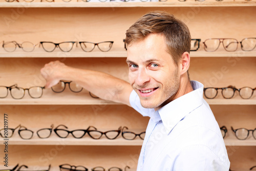 Okulary. Mężczyzna wybiera oprawki okularowe w salonie optycznym