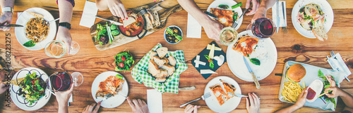 Family or friends summer party or outdoor dinner. Flat-lay of group of people at big table in cafe eating verious food together. Summer gathering or celebration concept