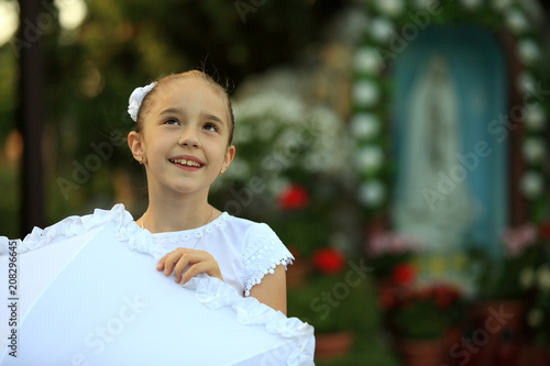 Śliczna mała dziewczynka w białej sukience przy chrześcijańskiej kapliczce.
