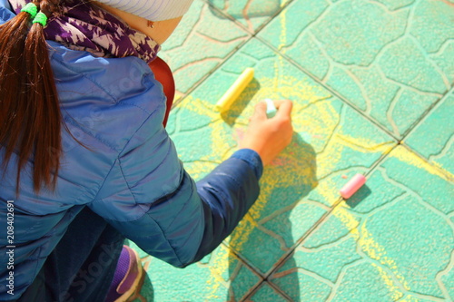 A little girl draws the sun with colored crayons on the road. Close-up. Background. Spring, May.
