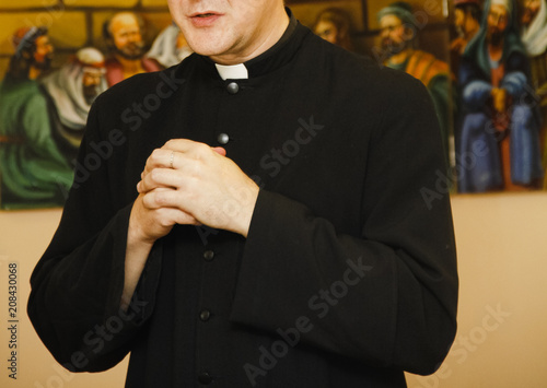 Priest in black cassock with clerical collar prays