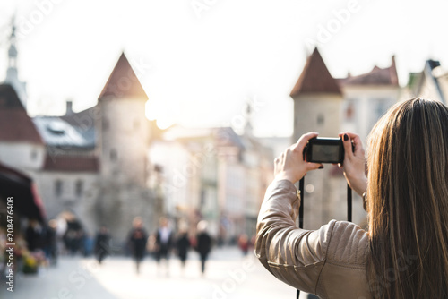 Woman in Tallinn taking photo of Viru Gate. Tourist on vacation taking picture of landmark in Estonia. People walking in popular street. Back view of girl with camera.
