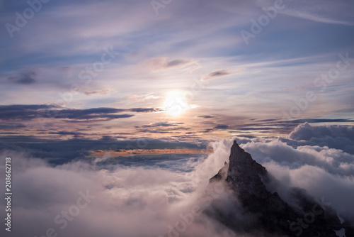 Landscape of mountain peaking over clouds, lit by sun