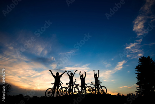 Friends with bikes at sunset background. Silhouettes of cyclists resting on evening sky background. Amazing summer evening scenery.